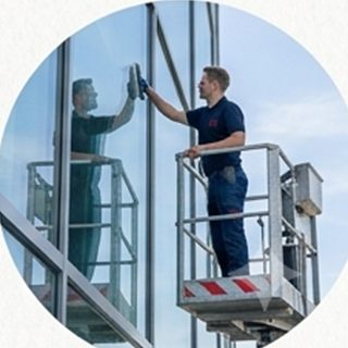 Mitarbeiter reinigt eine Glasfassade von einer Hubarbeitsbühne aus